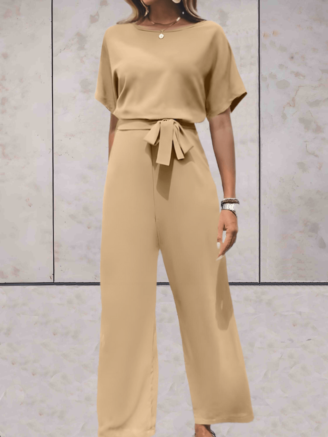 Eleganter Jumpsuit in Beige, schwarze Details, betont Silhouette, vielseitig für Tag und Abend, verfügbar in XS-2XL.